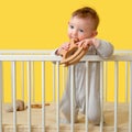 Sad toddler baby boy in the crib gnawing a wooden toy, yellow studio b Royalty Free Stock Photo