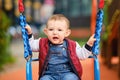 Sad toddler baby boy rides on a swing. A frightened child swings on th