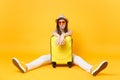 Sad traveler tourist woman in summer casual clothes, hat sit near suitcase on yellow orange background. Female Royalty Free Stock Photo