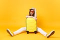 Sad traveler tourist woman in summer casual clothes, hat sit near suitcase on yellow orange background. Female Royalty Free Stock Photo