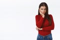 Sad troubled young brunette girl in red sweater, standing lonely and upset, hold hand on face, look from under forehead Royalty Free Stock Photo