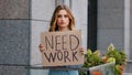 Sad unemployed blonde business woman stands in city looking at camera holds cardboard banner needs work job worried Royalty Free Stock Photo