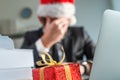 Sad and unhappy businessman with Santa Claus hat crying in office during Christmas holiday season