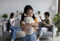 Sad unhappy despaired korean teenage girl hugs toy, parents quarrel and shout in living room interior, blurred Royalty Free Stock Photo