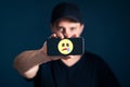 Sad unhappy emotion icon in phone. Depressed lonely man with smartphone. Online hate, trauma, cyber bullying. Royalty Free Stock Photo