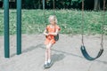 Sad unhappy girl is swinging on swing set in park outdoor alone. Upset bored kid waiting for friend on playground. Lonely child is Royalty Free Stock Photo