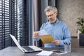 Sad unhappy man sitting at workplace inside office, senior mature gray-haired businessman taking mail letter, envelope Royalty Free Stock Photo