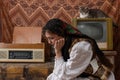 Sad, unhappy woman in national clothes sitting among vintage retro room. Royalty Free Stock Photo