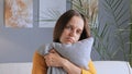 Sad unhappy worried bored woman sitting at home alone embracing pillow missing somebody being in bad mood looking at camera with