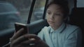 Sad, unhappy young boy riding in car through city during rainy day, using social network on his smartphone Royalty Free Stock Photo