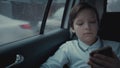 Sad, unhappy young boy riding in car through city during rainy day, using social network on his smartphone Royalty Free Stock Photo