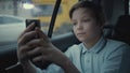 Sad, unhappy young boy riding in car through city during rainy day, using social network on his smartphone Royalty Free Stock Photo