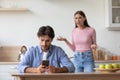 Sad unhappy young caucasian husband with smartphone ignoring upset angry scolding wife Royalty Free Stock Photo