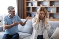 Sad upset angry adult european husband yells at unhappy wife, covers ears in living room interior Royalty Free Stock Photo