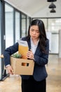 Sad and upset Asian female office worker is carrying a cardboard box and a resignation letter Royalty Free Stock Photo