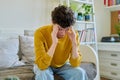 Sad upset young man sitting on couch at home, touching his head with hands Royalty Free Stock Photo