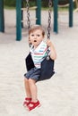 Sad upset worried little small boy toddler in tshirt and jeans shorts on swing on backyard playground