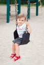 Sad upset worried little small boy toddler in tshirt and jeans shorts on swing on backyard playground Royalty Free Stock Photo