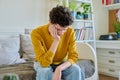 Sad upset young man sitting on couch at home, touching his head with hands Royalty Free Stock Photo