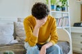 Sad upset young man sitting on couch at home, touching his head with hands Royalty Free Stock Photo