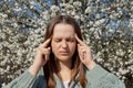 Sad upset young woman having allergy symptoms from blooming tree pollen in spring suffering terrible headache grimacing massaging Royalty Free Stock Photo