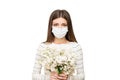 Sad upset young woman in medical white mask holding a bouquet of white lilac flowers.