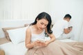 Sad view of young married couple using their mobile phone in bed ignoring each other as strangers in relationship and Royalty Free Stock Photo