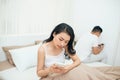 Sad view of young married couple using their mobile phone in bed ignoring each other as strangers in relationship and Royalty Free Stock Photo