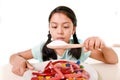Sad and vulnerable hispanic female child eating dish full of candy and gummies holding sugar spoon in wrong diet concept