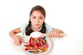 Sad and vulnerable hispanic female child eating dish full of candy and gummies holding sugar spoon in wrong diet concept Royalty Free Stock Photo