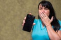 A sad woman with a broken phone put her hand on her face. The girl accidentally broke the screen of her smartphone. Hopeless