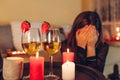 Sad woman crying at home by romantic table setting with wine glasses. Left alone and brokenhearted on Valentine's