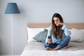 Sad woman in depression sitting at home on the couch with a mobile phone in her hands