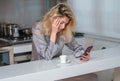 Sad woman drink coffee and using phone at home in morning. Tired female madel chatting smartphone in sexy pajama at