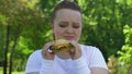 Sad woman eating burger with disgust, lack of willpower, fast food addiction