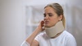 Sad woman in foam cervical collar talking phone suddenly feeling sharp neck pain