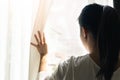 Sad woman holding the curtains open to look out of a large light window at home, interior Royalty Free Stock Photo