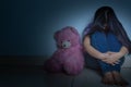 sad woman hug her knee and cry sitting with teddy bear in a dark room. Depression, unhappy, stressed and anxiety disorder concept