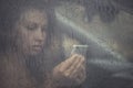 Sad woman looking in the mobile phone and reading message in the window with rain drop in the car. Royalty Free Stock Photo