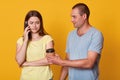 Sad woman looks down with upset expression while speaking via smart phone with her friend, standing with her husband against Royalty Free Stock Photo