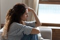 Sad young woman sitting on couch feels depressed side view