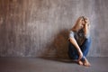 Sad woman sits on the floor. Depression and chronic fatigue. Young beautiful blonde in a gray sweater and jeans