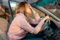 A sad woman is sitting behind the wheel of a car and holding her head with her hand. Royalty Free Stock Photo