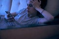 Sad woman surfing Internet or chatting using smartphone, lying on sofa at night. Concept of insomnia, addiction Royalty Free Stock Photo