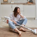 A sad woman with a wireless portable vacuum cleaner in the kitchen. A Royalty Free Stock Photo