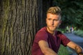 Sad, worried blond young man against tree