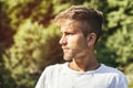 Sad, worried blond young man against trees