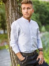 Sad, worried blond young man against tree