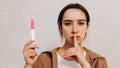 Sad worried girl holds a positive pregnancy test in her hands and shows the sign of silence. She does not want to know about her