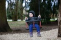 Sad, worried little boy swinging by himself, left alone unattended, looking for parents